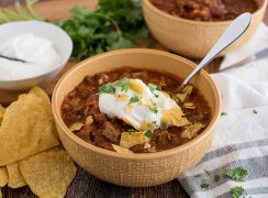 Beef and Bean Instant Pot Chili, dished up in a yellow serving bowl, with tortilla chips, sour cream, cheddar cheese, and cilantro