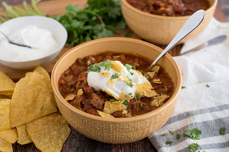 Beef and Bean Instant Pot Chili, dished up in a yellow serving bowl, with tortilla chips, sour cream, cheddar cheese, and cilantro