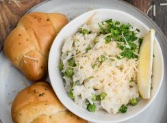 Close up overhead picture of lemon risotto made in an Instant Pot with peas, fresh parsley, parmesan, and a lemon wedge, next to some rolls.