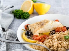 mediterranean fish on a white plate with brown rice and lemons