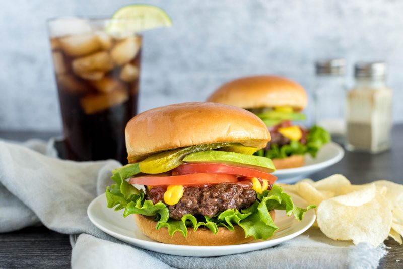 onion burgers on buns with toppings in front of a glass of soda