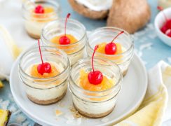 Four mini mason jars filled with mini tropical cheesecakes, topped with crushed pineapple topping and a maraschino cherry on top