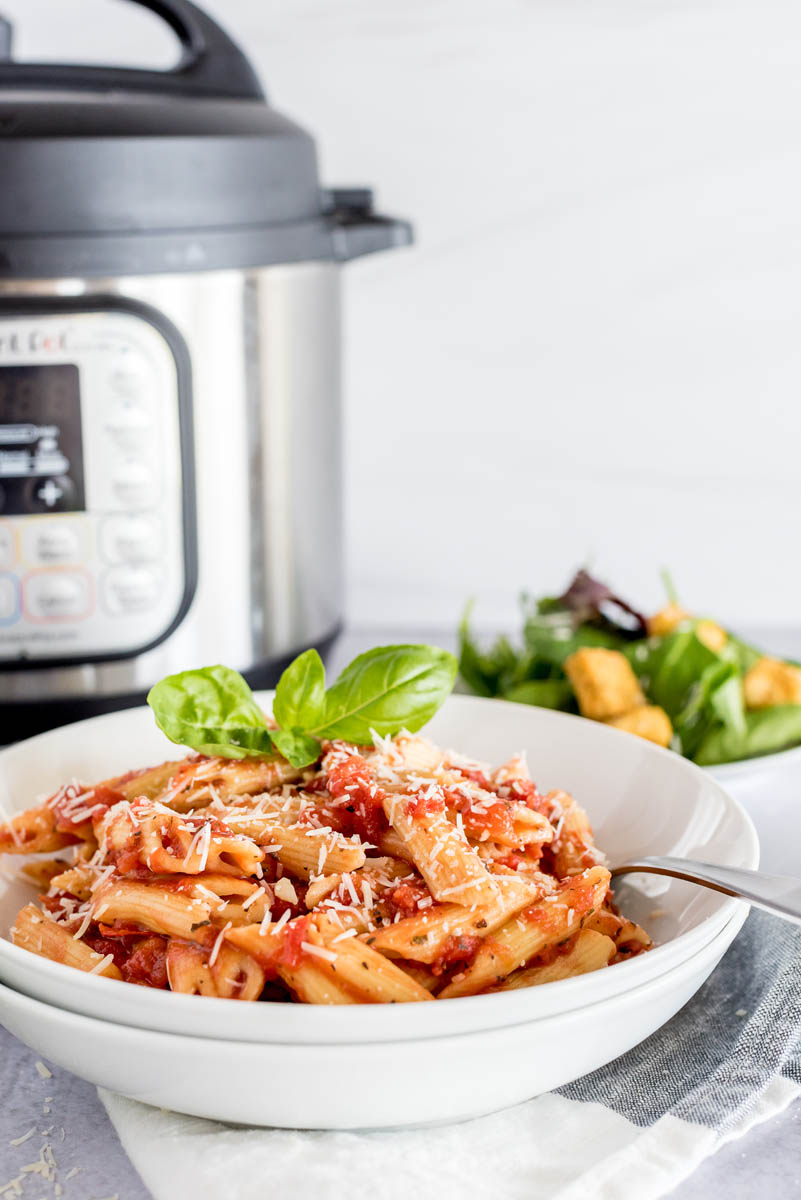 A close-up of the Quick Penne pasta in a white bowl, with a small tossed salad and an Instant Pot visible in the background