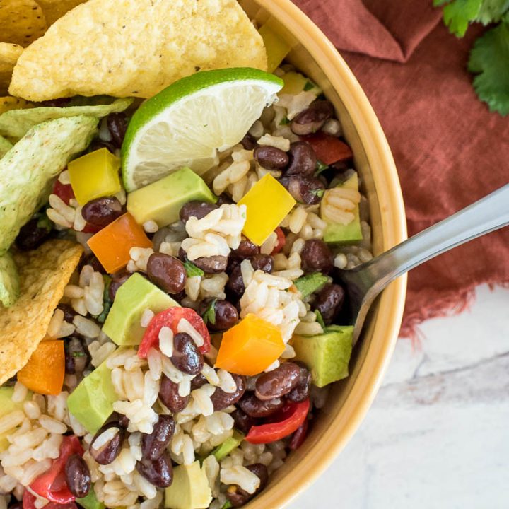 close up on a bowl of brown rice and black bean salad wth tortilla chips and lime