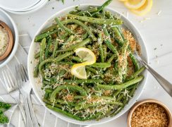 overhead shot of a white bowl of green beans with a lemon twist garnish and breadcrumbs