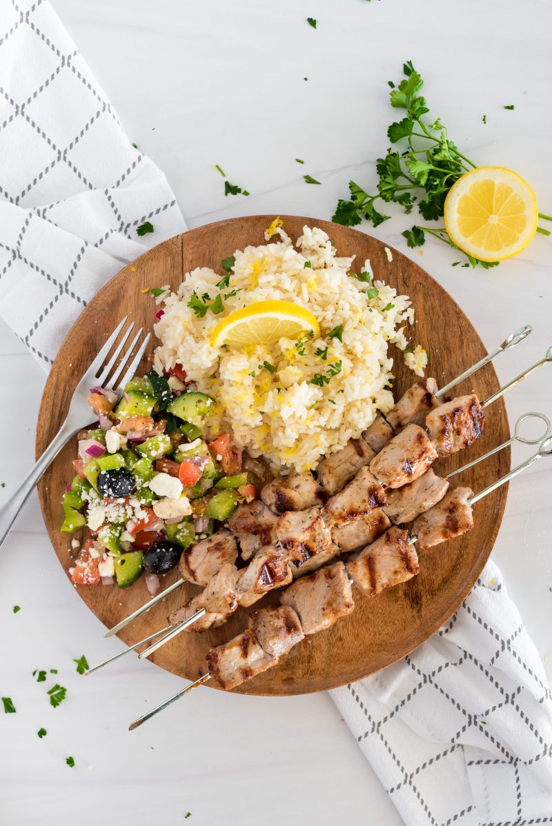 overhead of a wooden plate with lemon rice, chicken skewers and chopped salad