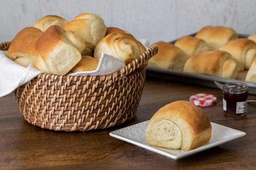 A basket of Lion House Rolls with on roll on a plate
