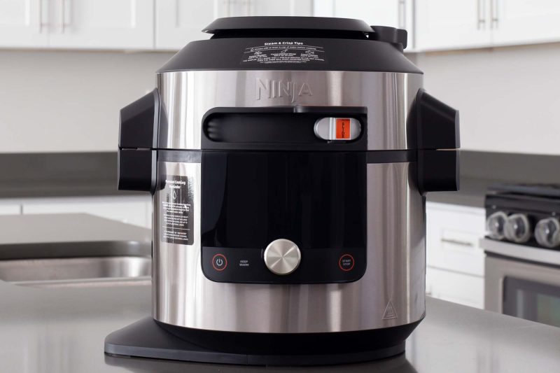 A direct head-on shot of the Ninja Foodi Smart XL Pressure COoker with SmartLid and Thermometer (model O701) sitting on a gray stone countertop with white cabinets in the background