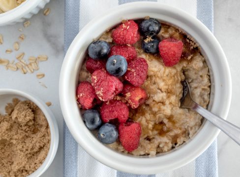 Close up shot of Instant Pot oatmeal for one topped with brown sugar, blueberries, and raspberries, with a bowl of brown sugar to the side.