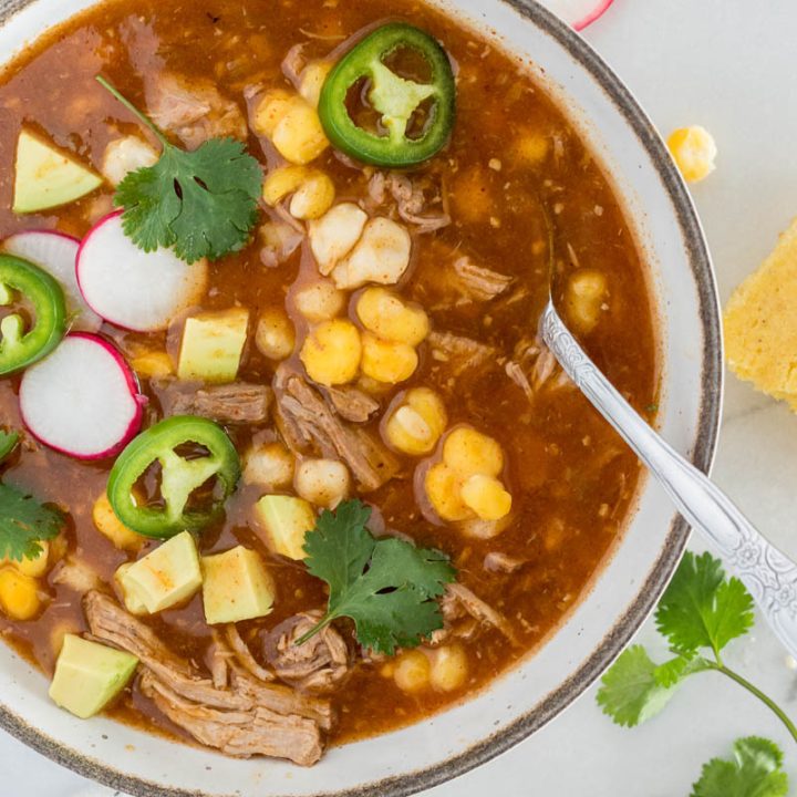 A close-up overhead shot of Instant Pot Posole stew with hominy and pork, garnished with cilantro, radishes, and peppers