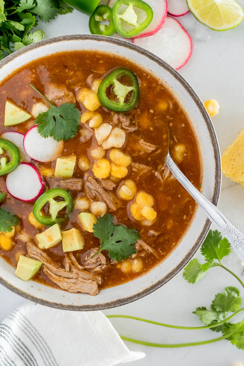 A close-up overhead shot of Instant Pot Posole stew with hominy and pork, garnished with cilantro, radishes, and peppers