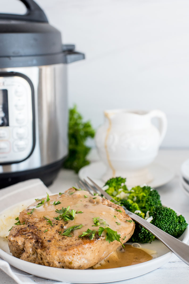 plate of pork chops with mushroom gravy in front of an electric pressure cooker