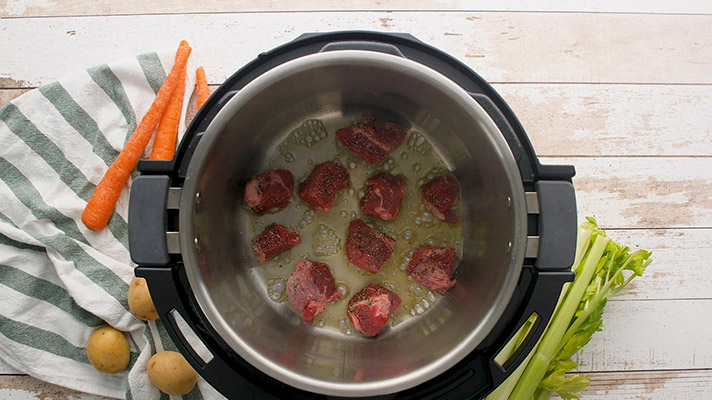 Overhead shot of cubed beef browning inside the cooking pot of an Instant Pot.