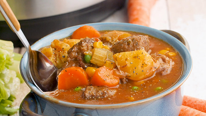 A bowl of pressure cooker beef stew ready sto serve with a spoon.