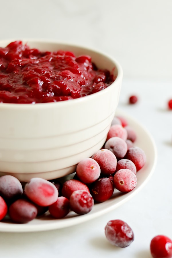 plate of fresh cranberries garnishes a white bowl of Instant Pot Cranberry Apple Sauce