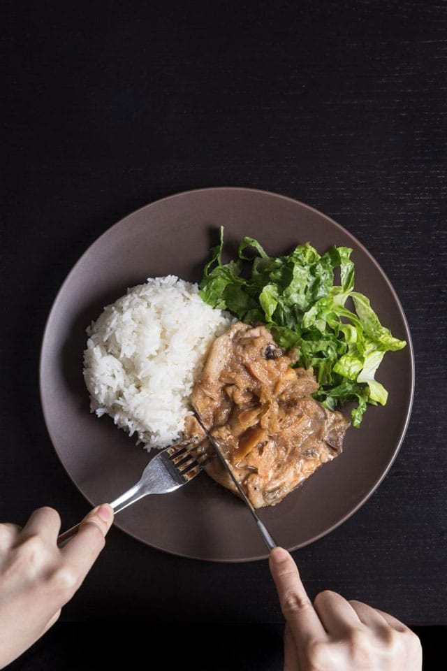 brown dinner plate with pork chops made in a pressure cooker, along with white rice and a green salad