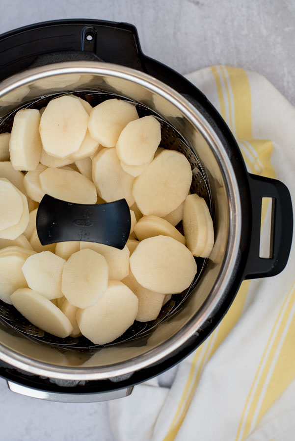 Easy scalloped potatoes ready to cook in a steam basket placed inside an Instant Pot.
