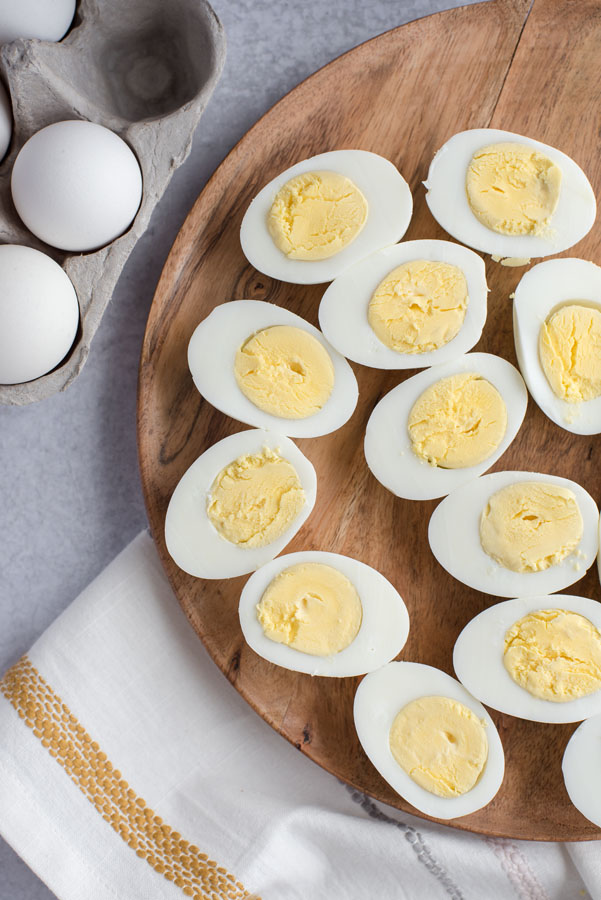 Overhead of a round wooden board with many perfectly cooked Instant Pot hard-boiled eggs cut in half with yellow yolks and firm egg whites.