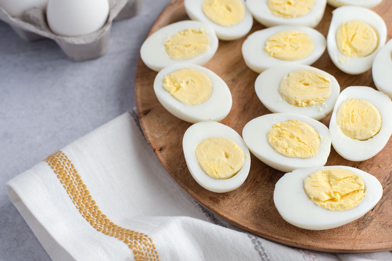 OVerhead of a round wooden board with Instant Pot hard-boiled eggs cut in half on a white and yellow striped dishcloth.
