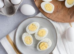 Overhead of a grey ceramic plate with four halves of perfectly cooked Instant Pot / pressure cooker hard-boiled eggs sprinkled with salt and black pepper on a white, grey and yellow striped cloth dishtowel.