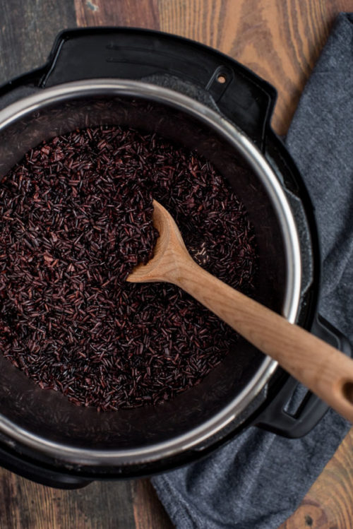 Black rice after pressure cooking in the Instant Pot, inside the cooking pot with a wooden spoon for stirring