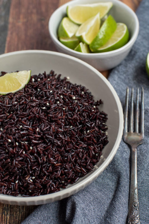 Pressure Cooker / InstaPot Black Rice garnished with limes and sesame seeds, served on a napkin with a fork