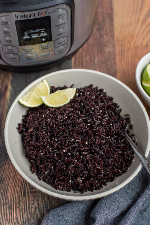 A white bowl full of Pressure Cooker Black Rice, shot from above, with an Instant Pot and limes in the background