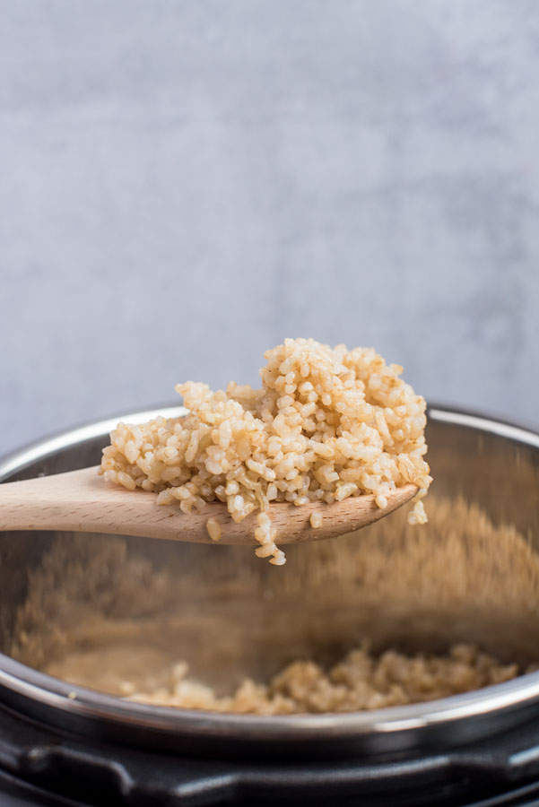 Pressure Cooker Brown Rice scooped on a wooden spoon with the Instant Pot cooking pot in the background