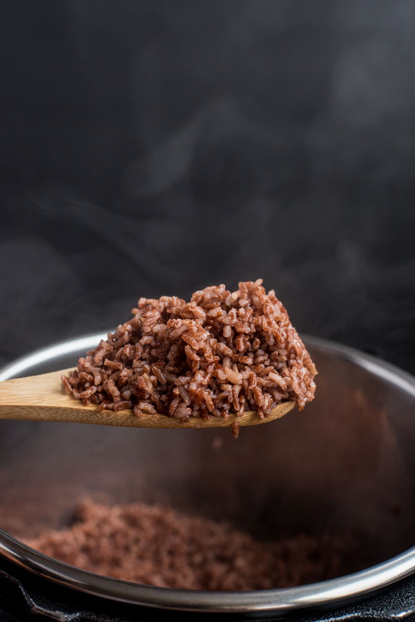 A spoonful of prepared Instant Pot pink rice, with steam rising from the spoon.