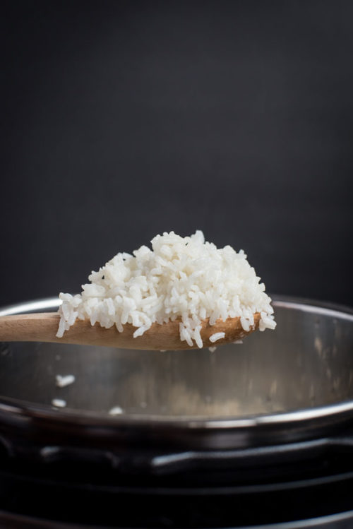 A wooden spoonful of Pressure Cooker White Rice, lifting out of the Instant Pot