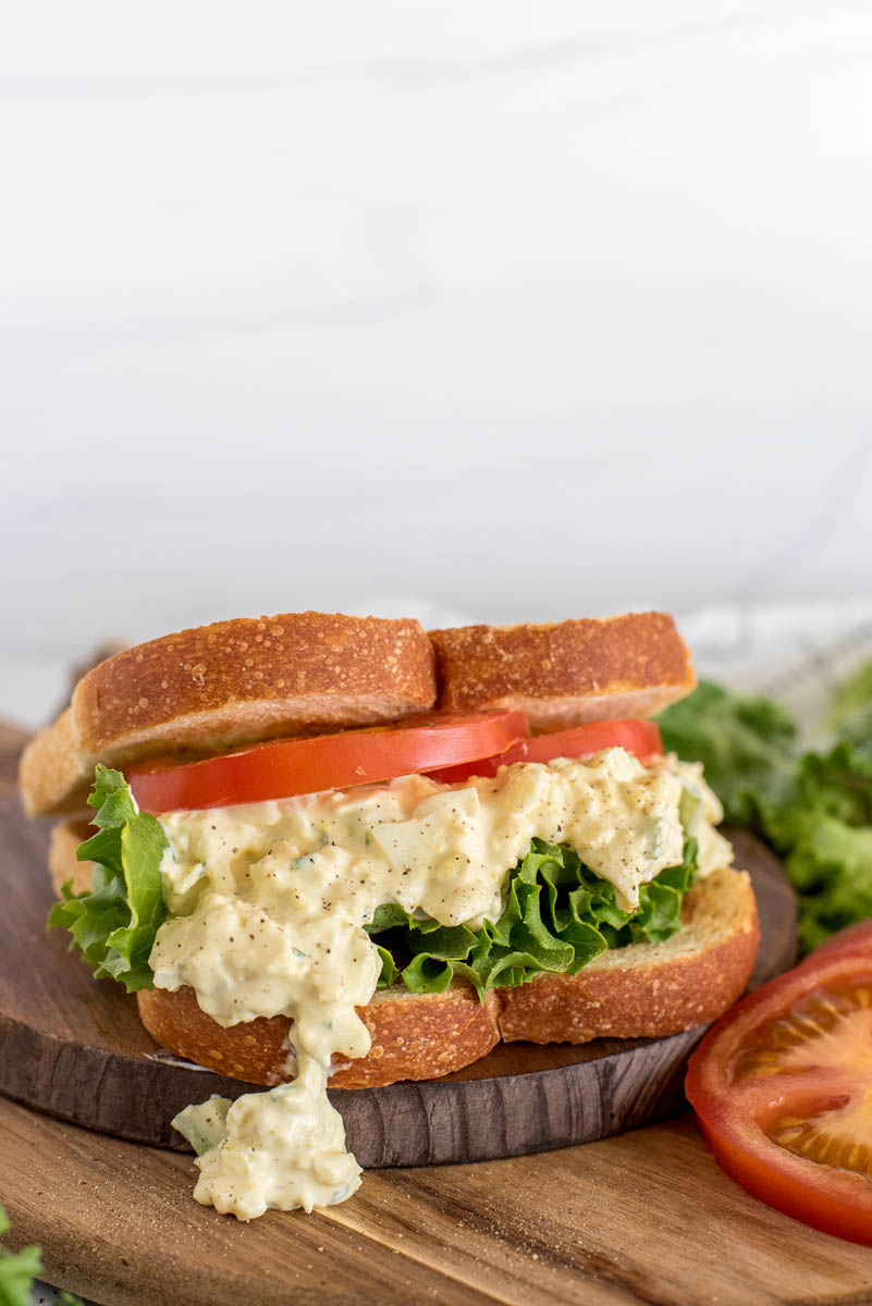 Instant Pot egg salad sandwich made on toasted bread with sliced tomatoes and lettuce. Placed on top of a wooden cutting board.