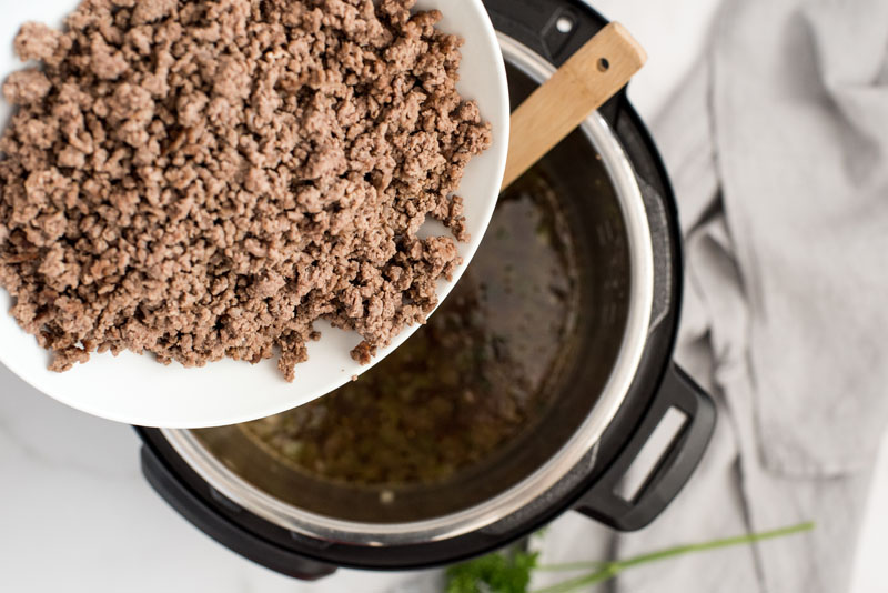 adding cooked ground beef to an instant pot to make american chop suey