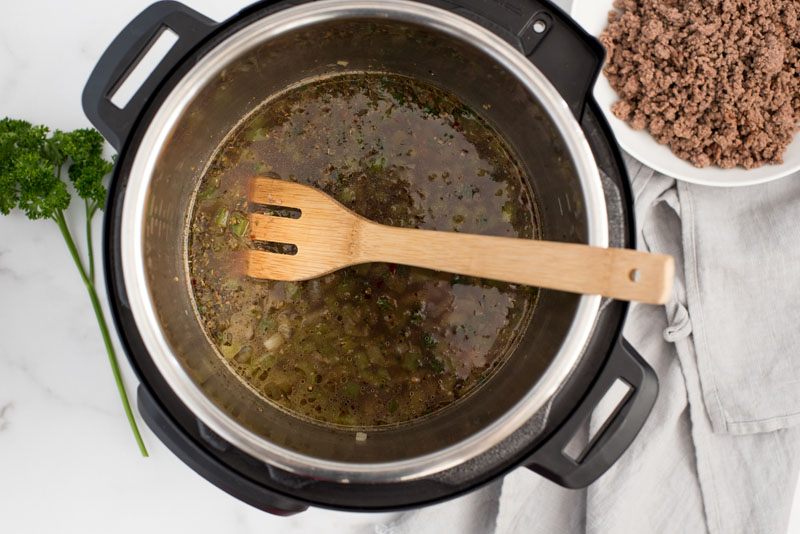overhead image of an Instant Pot with wooden spoon and brown sauce inside