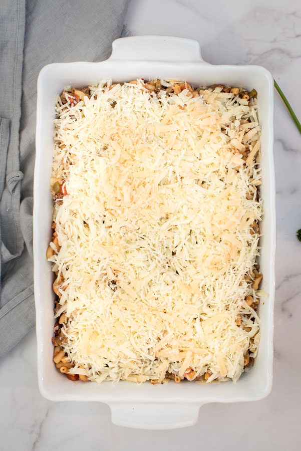 overhead of a white ceramic baking dish with Instant Pot beefaroni casserole covered with shredded Mozzarella cheese, ready for baking
