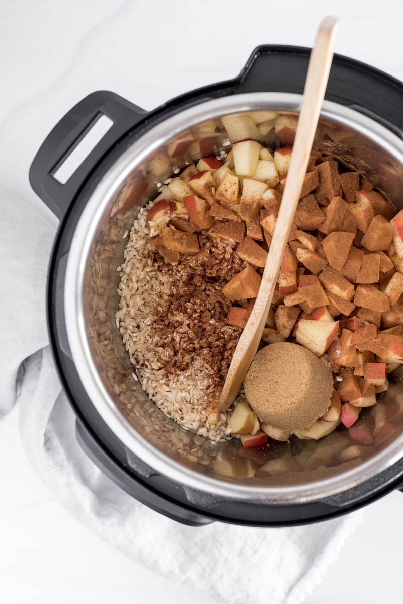 An overhead shot of all of the ingredients, including brown sugar, diced apples, cherries, cinnamon, and arborio rice, looking down into the Instant Pot cooking pot