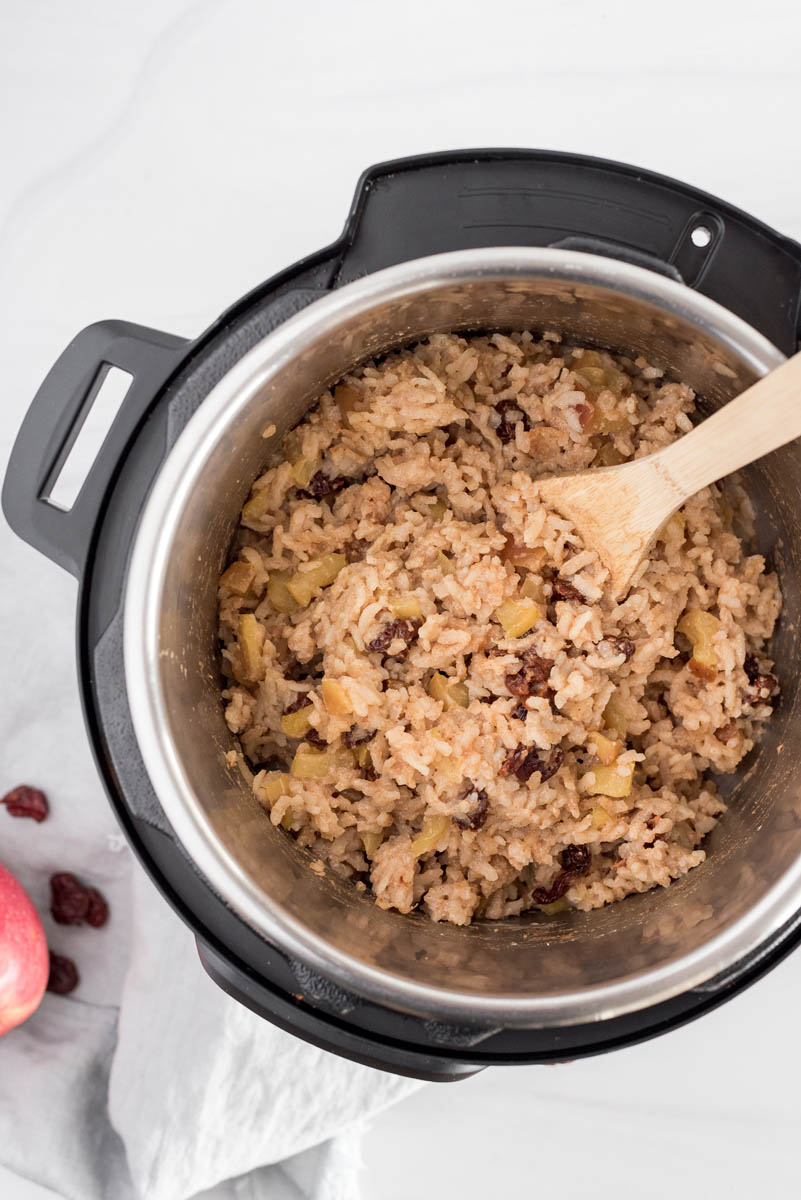 An overhead shot looking into an Instant Pot Duo Nova, with the cooked Instant Pot Apple Risotto cooked and ready to scoop into serving bowls with a wooden spoon