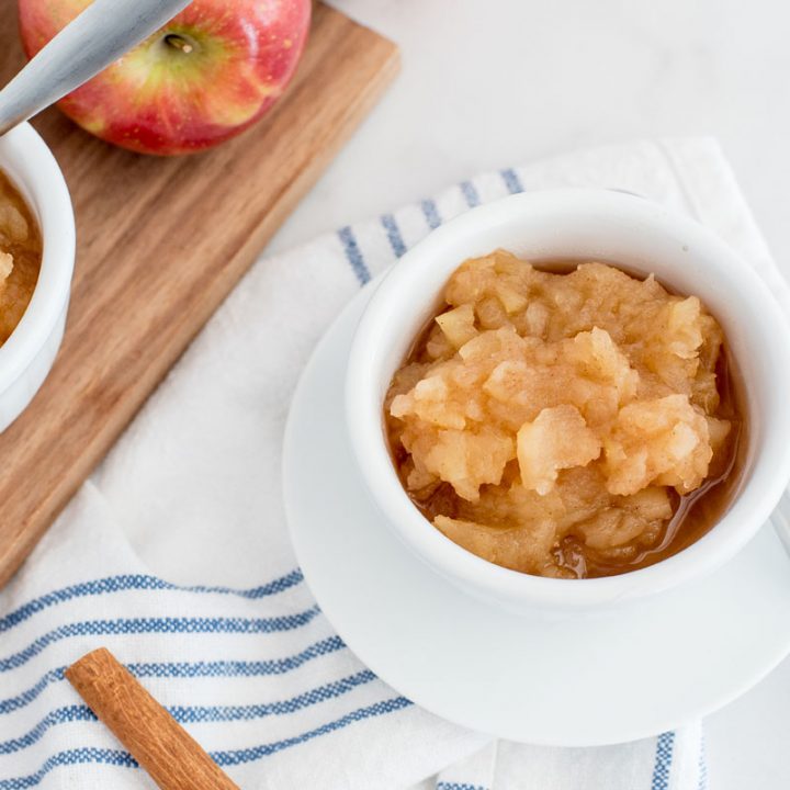 instant pot apple sauce in a small white dish with a wooden board behind