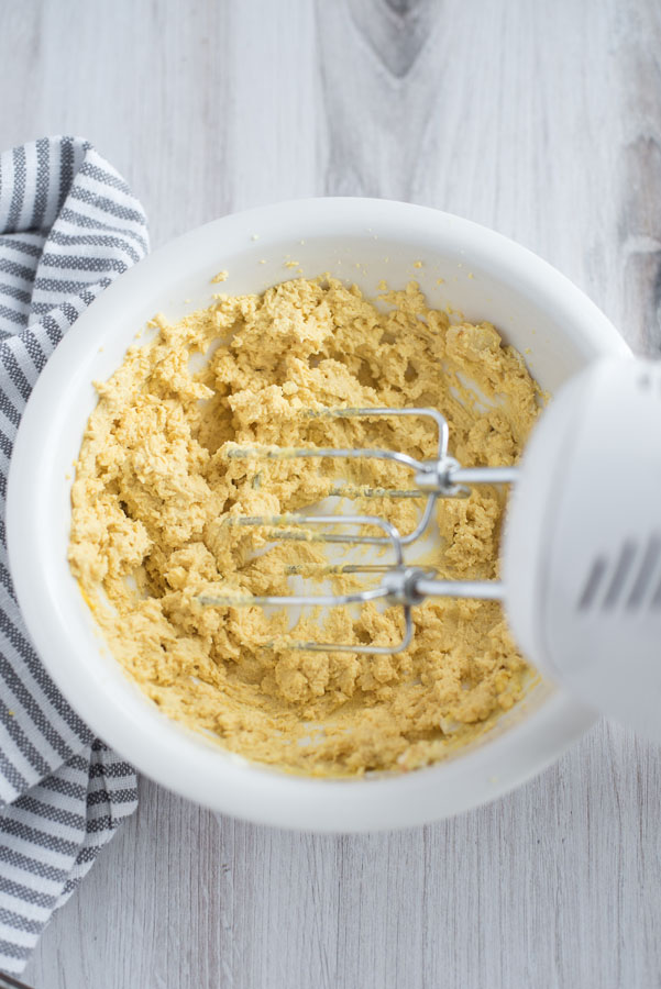 Overhead of a hand mixer stirring up egg yolks with mustard, greek yogurt, and mayonnaise to make Instant Pot deviled eggs.