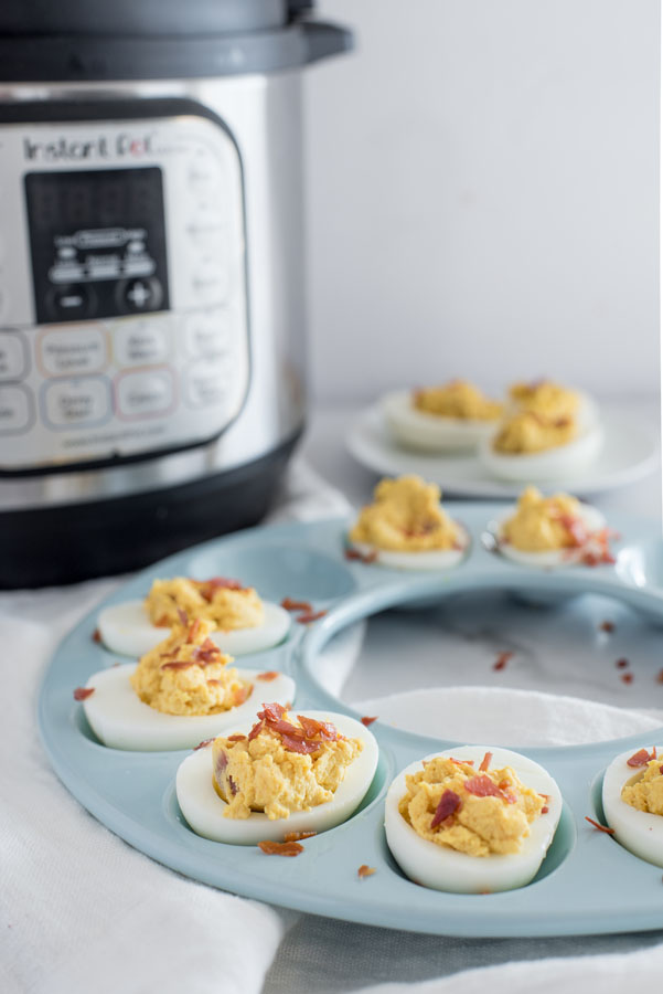 Close up on a blue egg tray filled with Instant Pot Barbecue Deviled Eggs with Bacon with an Instant Pot in the background.