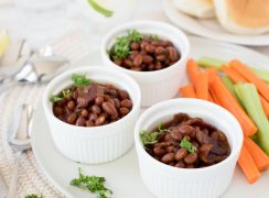 Three white ramekins filled with Instant Pot baked beans served with celery and carrot sticks on the side