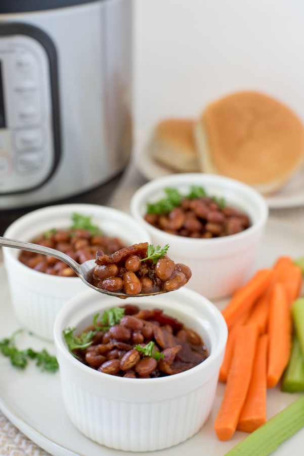 Instant pot baked beans in white ramekins with a spoonful being taken ou