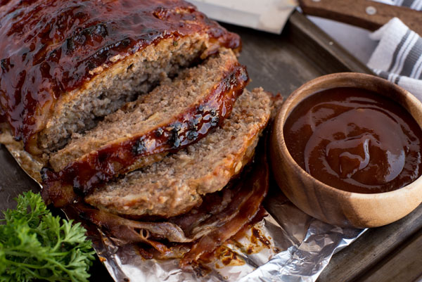 Close up of sliced pressure cooker BBQ bacon meat loaf with a bowl of BBQ sauce for serving.