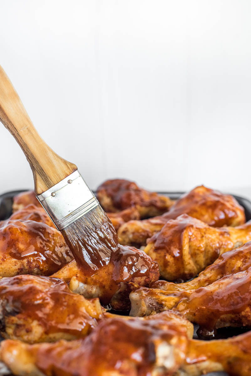 A close-up of a brush applying barbecue sauce to the chicken legs.