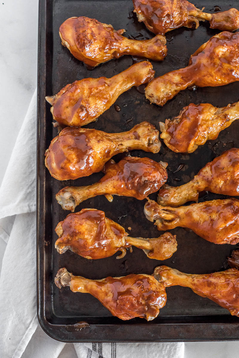 Cooked chicken legs on a dark baking sheet, covered in BBQ sauce