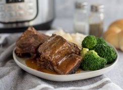 Bone-in pressure cooker Short Ribs plated with broccoli and mashed potatoes in front of an Instant Pot.