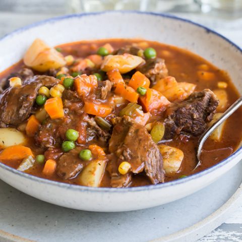 A bowl of Pressure Cooker Beef Stew with chunky potatoes, carrots, and peas in a bowl with a spoon.