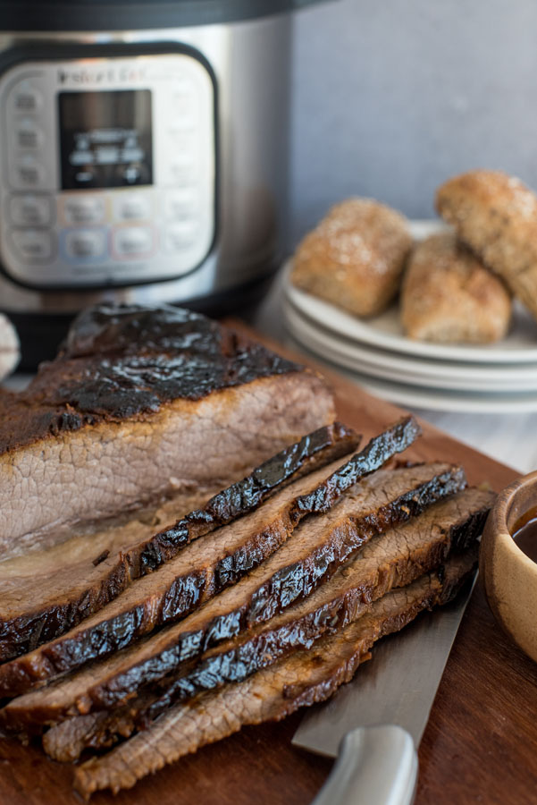 Beef brisket sliced on a cutting board in front of an Instant Pot