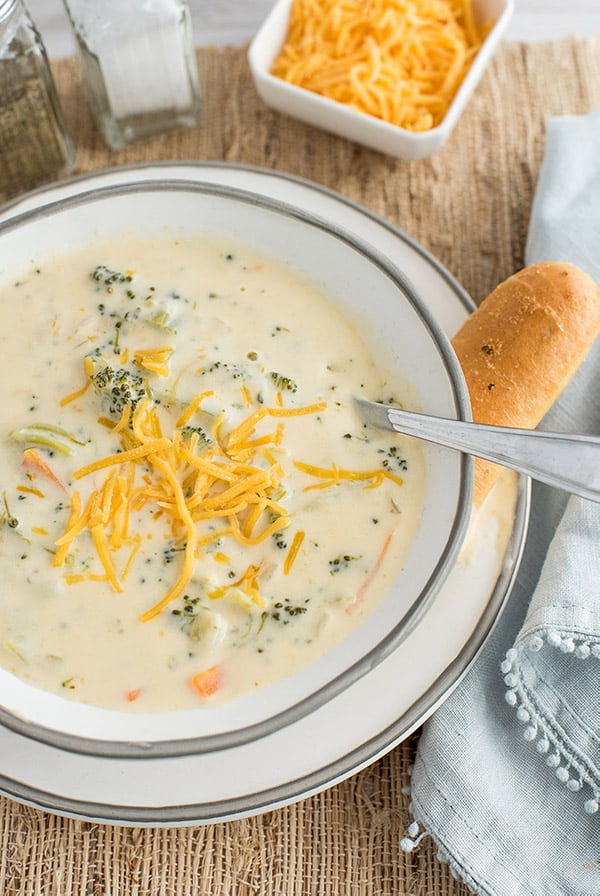 Instant Pot / Pressure Cooker Broccoli Cheese Soup in a white bowl with a spoon in it and a bread stick on the side