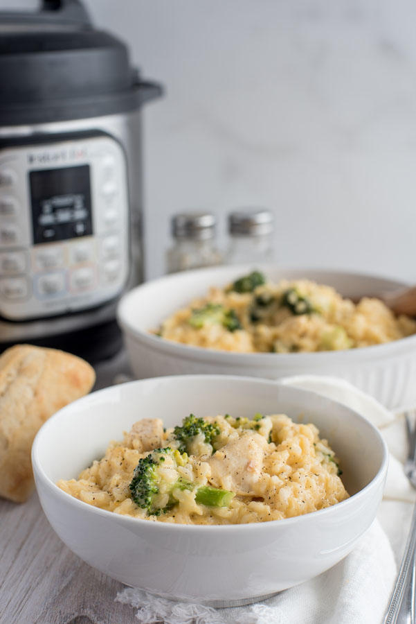 Cheesy chicken and broccoli in a white bowl with an Instant Pot in the background.