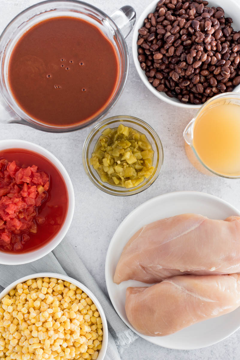 Overhead of all of the ingredients for quick and easy Instant Pot Chicken Enchilada Soup: enchilada sauce, mild green chiles, black beans, chicken stock, chicken breasts, frozen corn, and diced canned tomatoes.